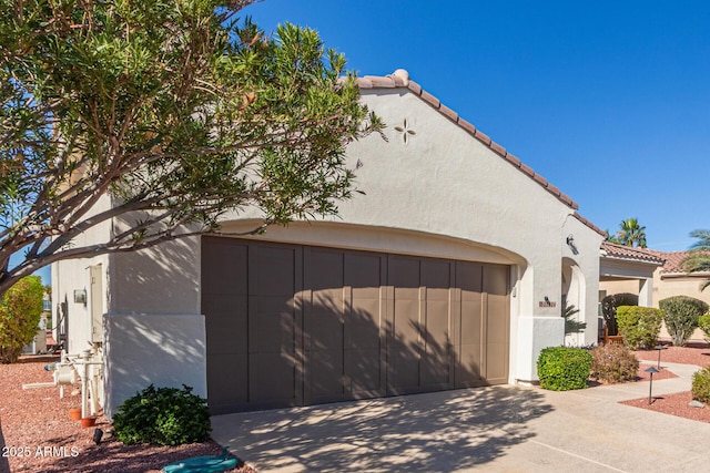 view of property exterior with driveway, a tile roof, an attached garage, and stucco siding