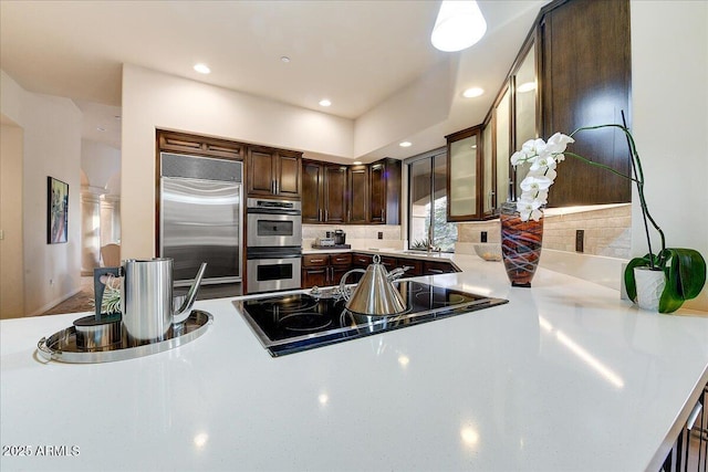 kitchen with appliances with stainless steel finishes, sink, backsplash, kitchen peninsula, and dark brown cabinets