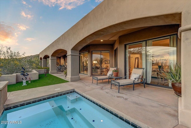 pool at dusk with a hot tub and a patio