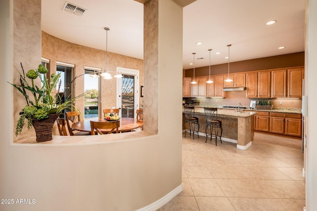 interior space featuring light tile patterned floors, decorative light fixtures, a breakfast bar area, and a center island