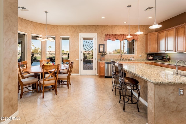 kitchen featuring a breakfast bar, decorative light fixtures, dishwasher, sink, and light stone countertops