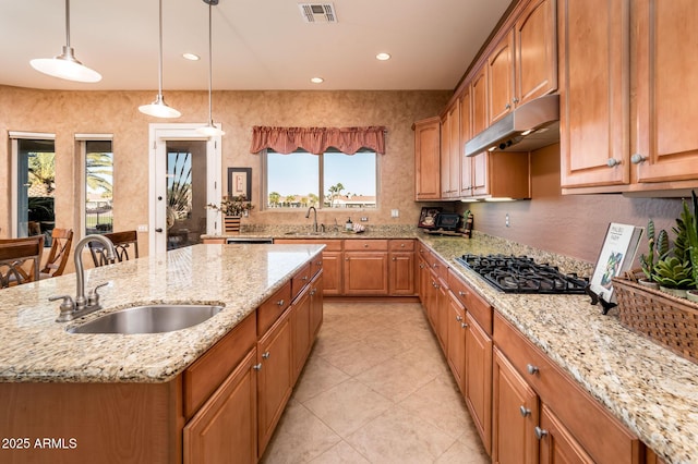 kitchen featuring decorative light fixtures, sink, a kitchen island with sink, black gas stovetop, and light stone countertops