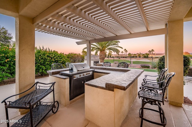 patio terrace at dusk with a grill, a pergola, and exterior kitchen