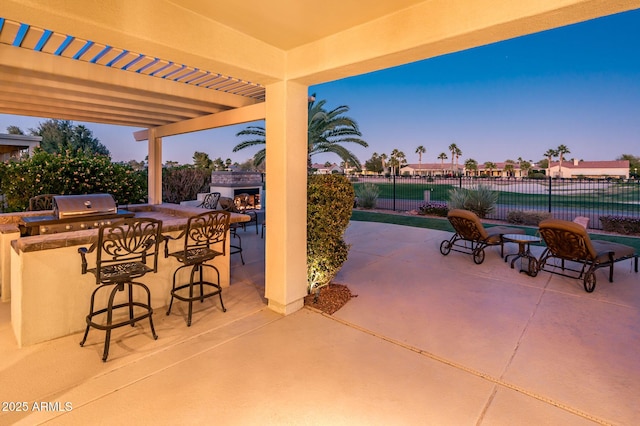 patio terrace at dusk featuring a bar, an outdoor kitchen, and area for grilling