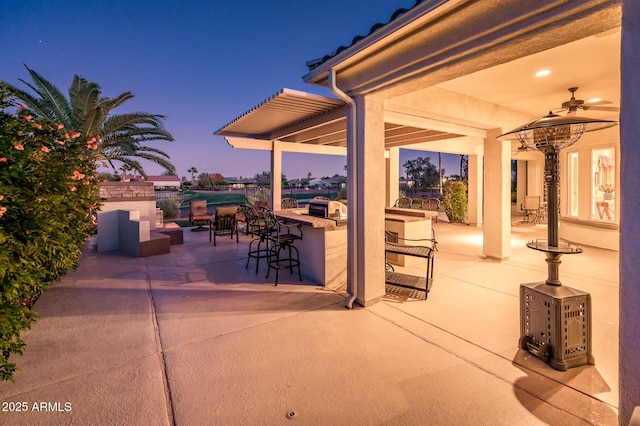 patio terrace at dusk featuring an outdoor bar, ceiling fan, and an outdoor kitchen