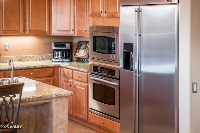 kitchen featuring light tile patterned flooring, appliances with stainless steel finishes, light stone countertops, and sink