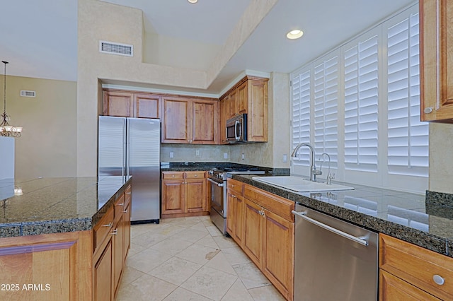kitchen featuring brown cabinets, stainless steel appliances, tile countertops, a sink, and an inviting chandelier