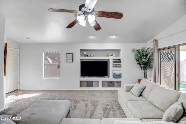 living room featuring built in shelves, ceiling fan, carpet flooring, and vaulted ceiling