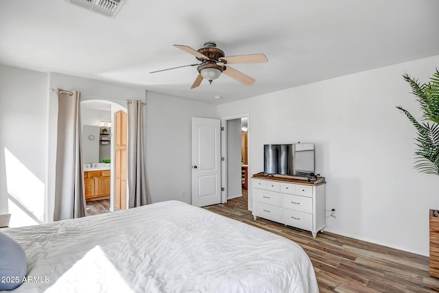 bedroom featuring visible vents, ensuite bathroom, wood finished floors, arched walkways, and ceiling fan