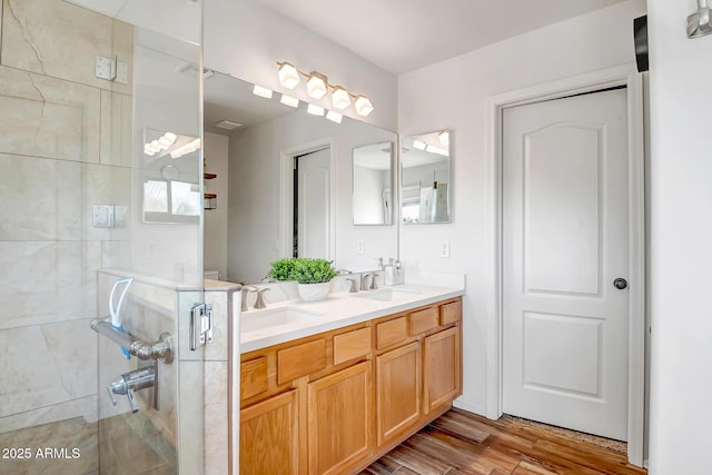 bathroom featuring a sink, wood finished floors, a stall shower, and double vanity