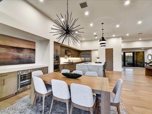 dining area with a notable chandelier, sink, wine cooler, and light hardwood / wood-style floors