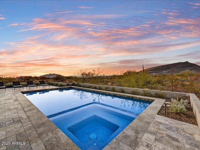 pool at dusk featuring an in ground hot tub and a patio