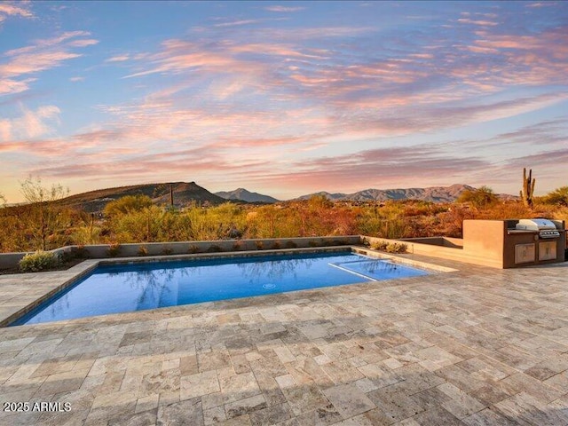 pool at dusk featuring a mountain view, a patio, and an outdoor kitchen