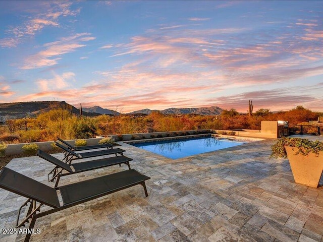 pool at dusk featuring a patio and a mountain view