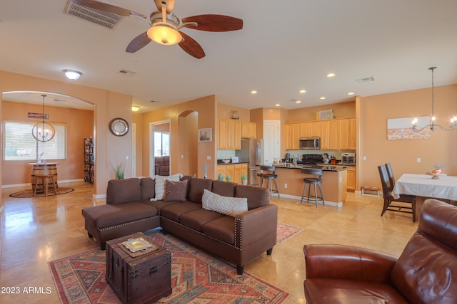 tiled living room with ceiling fan with notable chandelier