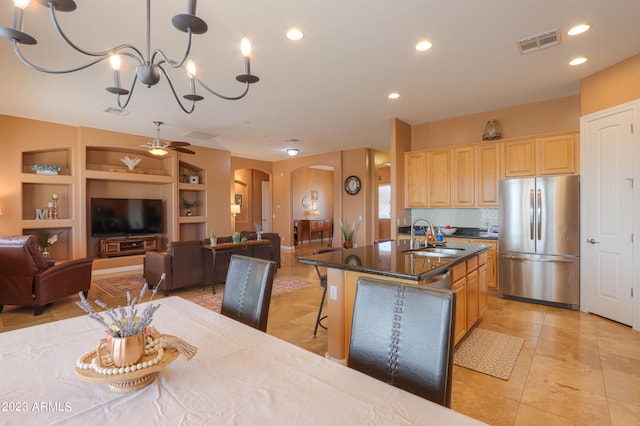 kitchen featuring light brown cabinets, a kitchen island with sink, sink, built in shelves, and stainless steel refrigerator