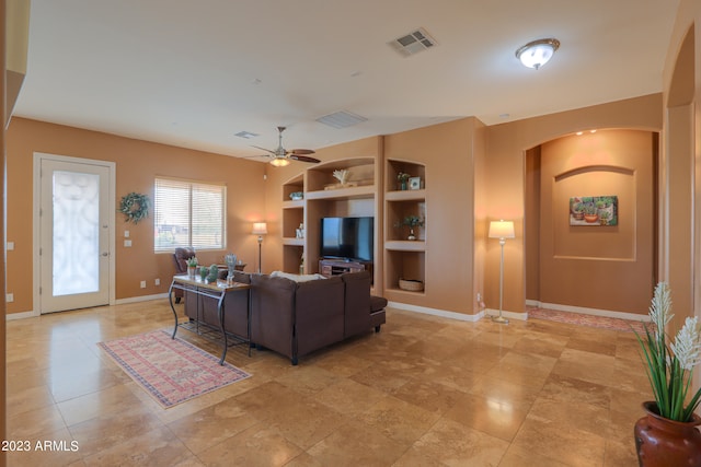 living room with built in shelves and ceiling fan