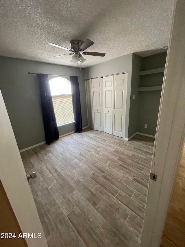 unfurnished bedroom with ceiling fan, a textured ceiling, and light wood-type flooring