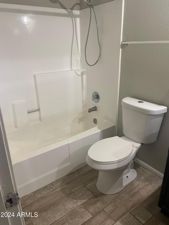 bathroom featuring hardwood / wood-style flooring, shower / washtub combination, and toilet