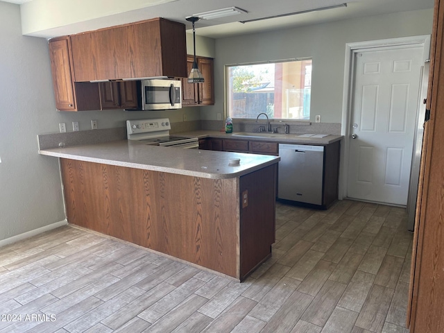 kitchen with stainless steel appliances, sink, kitchen peninsula, hanging light fixtures, and light wood-type flooring