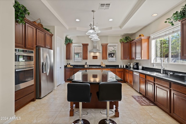 kitchen featuring a kitchen island, wall chimney exhaust hood, hanging light fixtures, a raised ceiling, and appliances with stainless steel finishes