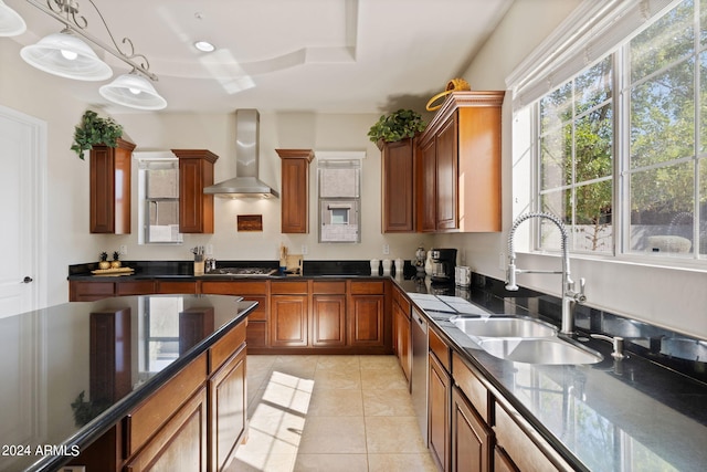 kitchen with wall chimney range hood, sink, stainless steel appliances, pendant lighting, and light tile patterned floors