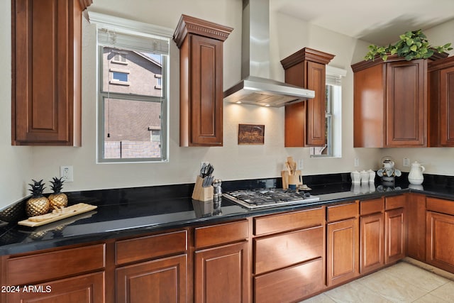 kitchen featuring stainless steel gas stovetop, light tile patterned flooring, wall chimney range hood, and dark stone countertops