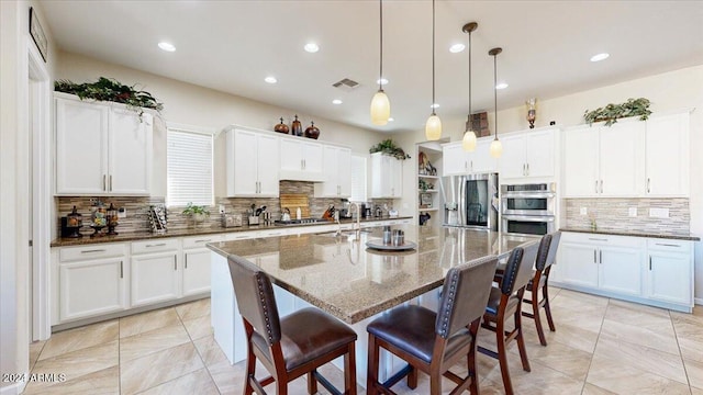 kitchen with white cabinetry, tasteful backsplash, pendant lighting, a kitchen island with sink, and appliances with stainless steel finishes