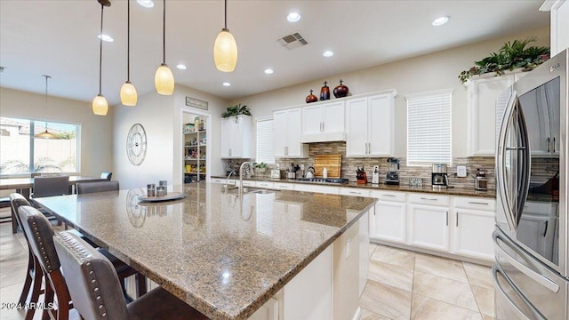 kitchen featuring appliances with stainless steel finishes, a kitchen island with sink, sink, decorative light fixtures, and white cabinetry