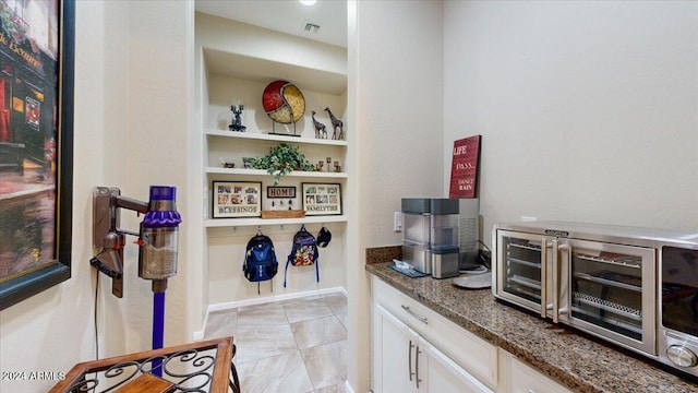 bar with white cabinets and dark stone countertops