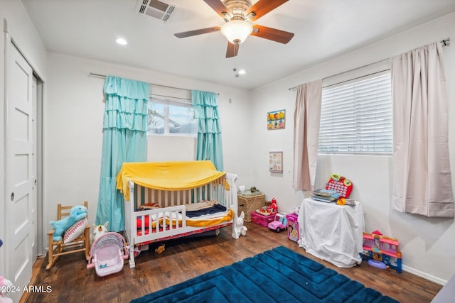 bedroom featuring a crib, dark hardwood / wood-style flooring, and ceiling fan