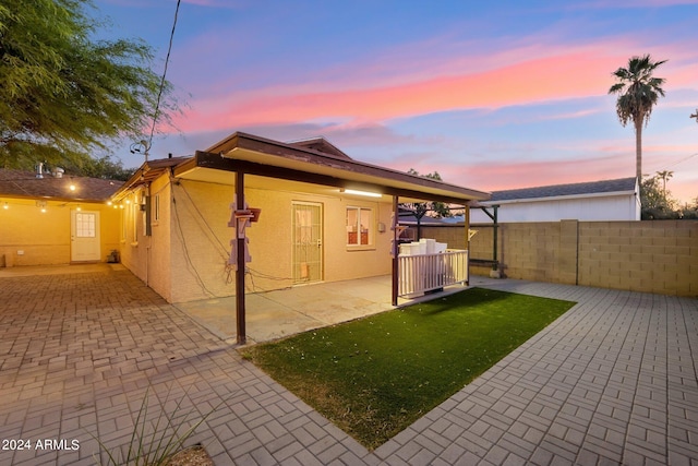 back house at dusk featuring a lawn and a patio