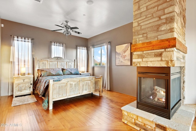 bedroom with wood-type flooring, ceiling fan, and a stone fireplace