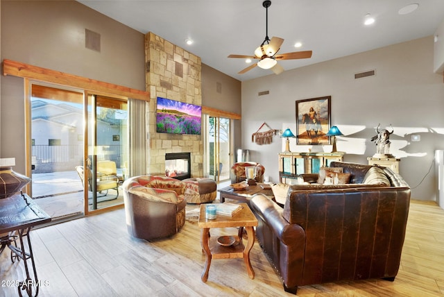 living room featuring a towering ceiling, a fireplace, ceiling fan, and light wood-type flooring