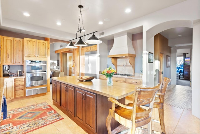 kitchen featuring decorative light fixtures, stainless steel appliances, light tile patterned floors, custom range hood, and decorative backsplash