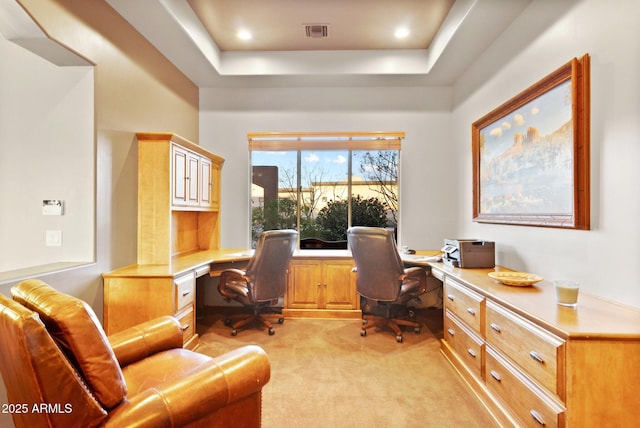 home office with built in desk, a tray ceiling, and light carpet