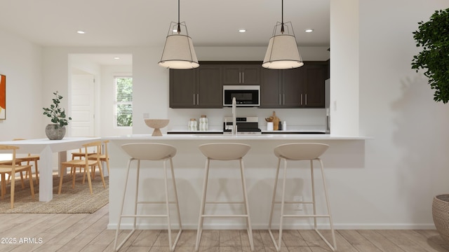 kitchen with light wood-style floors, stainless steel microwave, stove, and a kitchen bar