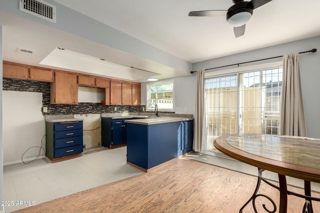 kitchen with sink, light wood-type flooring, a tray ceiling, ceiling fan, and decorative backsplash