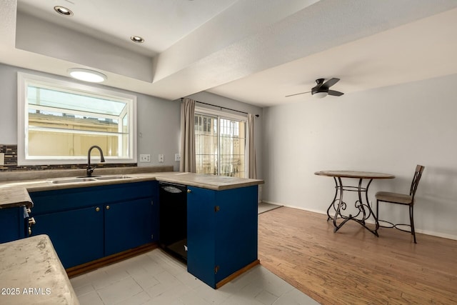 kitchen featuring sink, kitchen peninsula, a raised ceiling, blue cabinetry, and light wood-type flooring