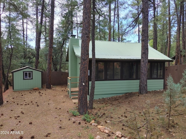 exterior space with a chimney, a storage shed, a sunroom, fence, and metal roof