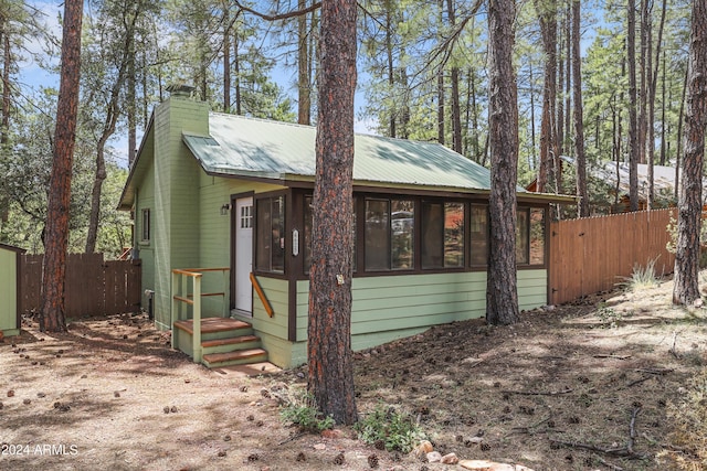 view of front of home with entry steps, metal roof, a chimney, and fence