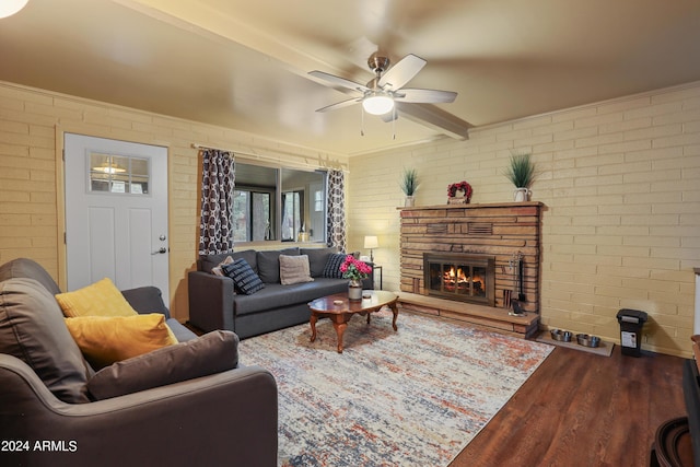 living area featuring ceiling fan, brick wall, dark wood-type flooring, and a stone fireplace