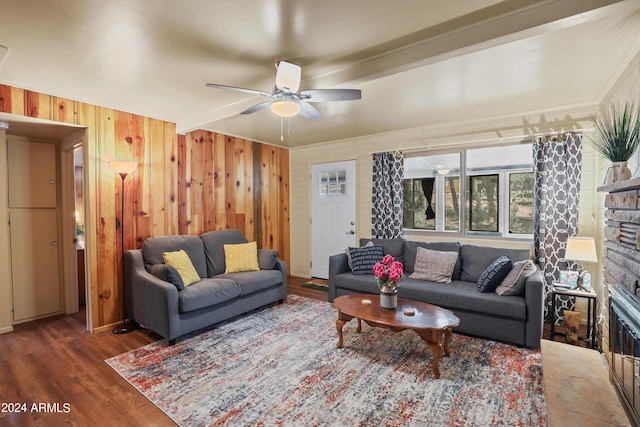 living room featuring a ceiling fan, dark wood finished floors, a stone fireplace, and wooden walls