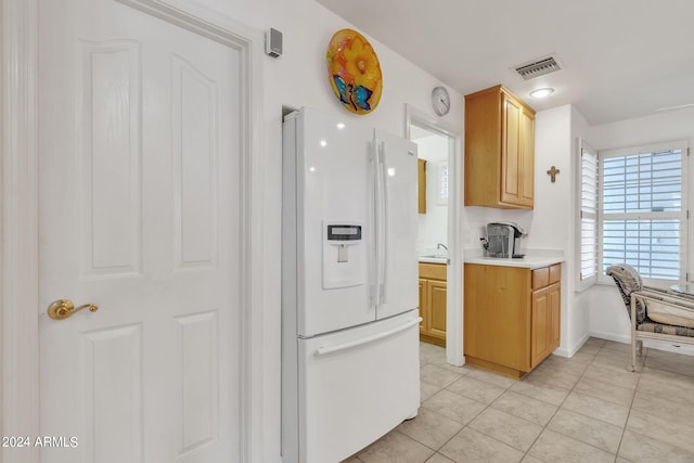 kitchen with white fridge with ice dispenser, light tile patterned flooring, and light brown cabinetry