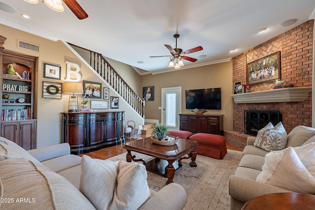 living room featuring a brick fireplace, crown molding, light hardwood / wood-style flooring, and ceiling fan