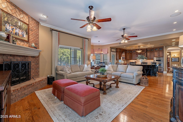 living room featuring crown molding, a fireplace, light hardwood / wood-style floors, and ceiling fan with notable chandelier