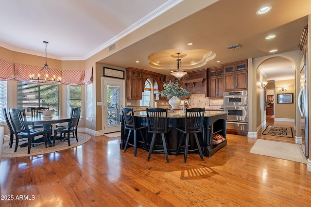 kitchen featuring ornamental molding, light stone countertops, decorative light fixtures, stainless steel double oven, and light wood-type flooring