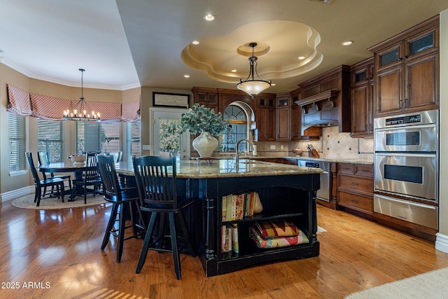 kitchen featuring double oven, backsplash, hanging light fixtures, light stone countertops, and light hardwood / wood-style flooring