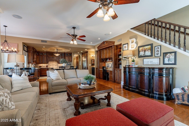 living room featuring ceiling fan with notable chandelier, ornamental molding, and light hardwood / wood-style floors