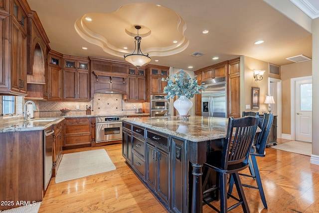 kitchen with sink, decorative light fixtures, appliances with stainless steel finishes, a kitchen island, and light stone countertops